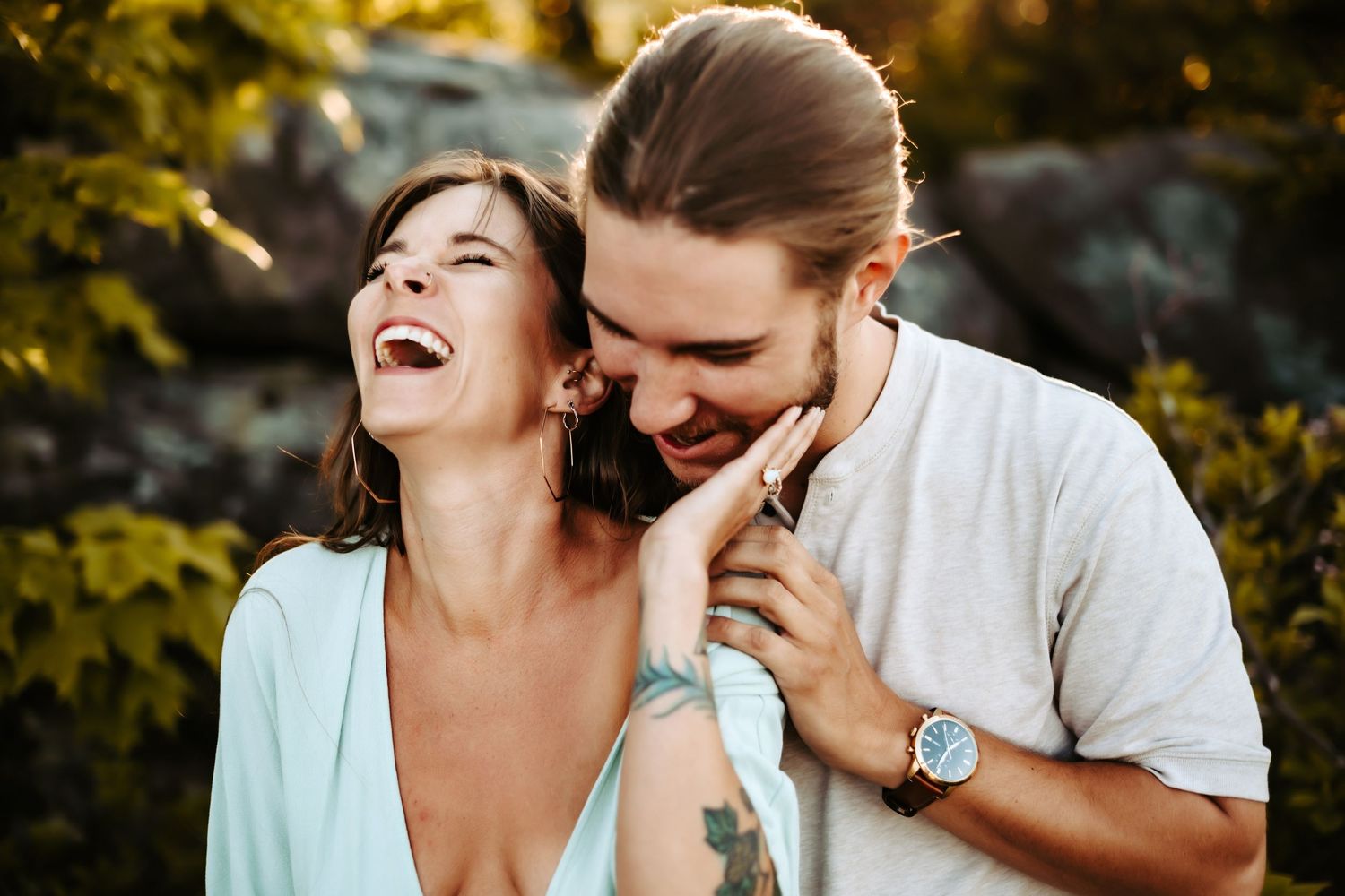 A joyful couple laughing together outdoors with golden sunlight filtering through trees in the background.