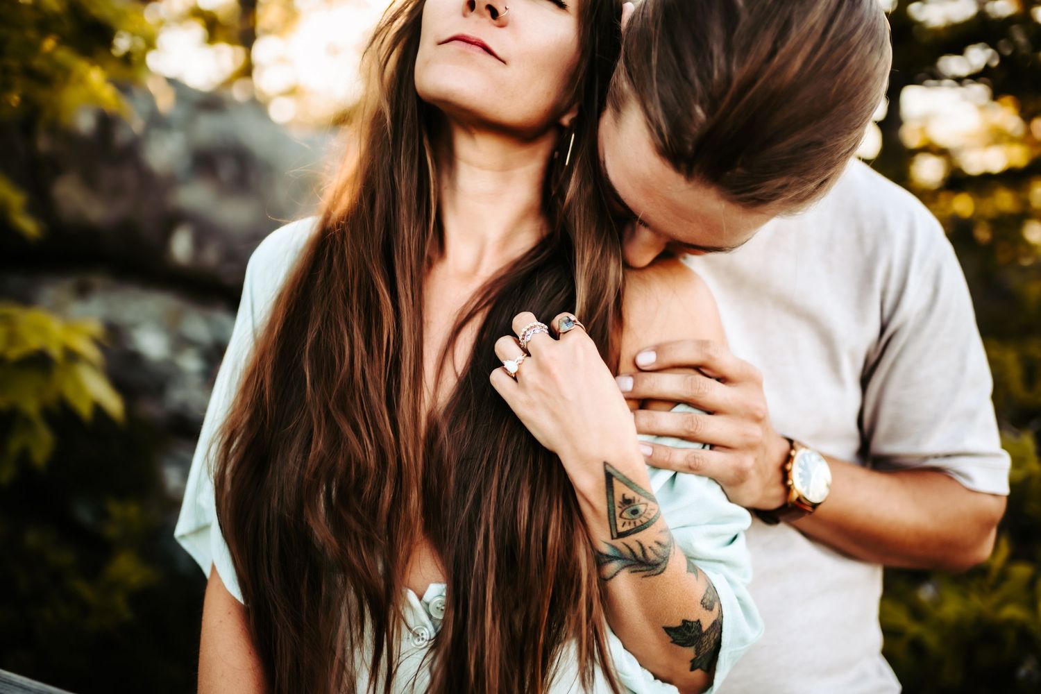 Close-up outdoors shot showing affectionate moment with visible tattoos and long flowing hair.