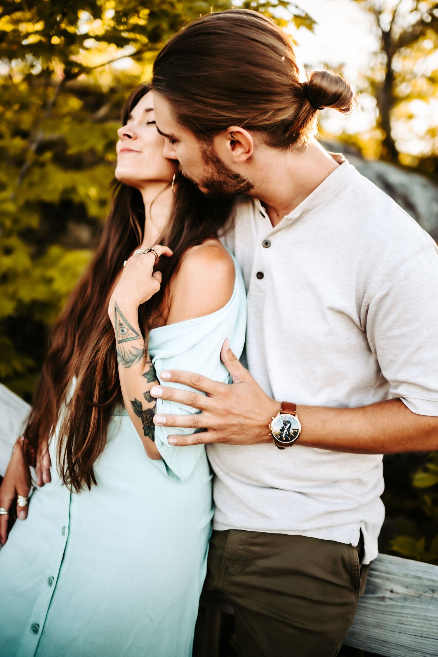 Romantic couple embraces in a tender moment at sunset with autumn foliage in the background.
