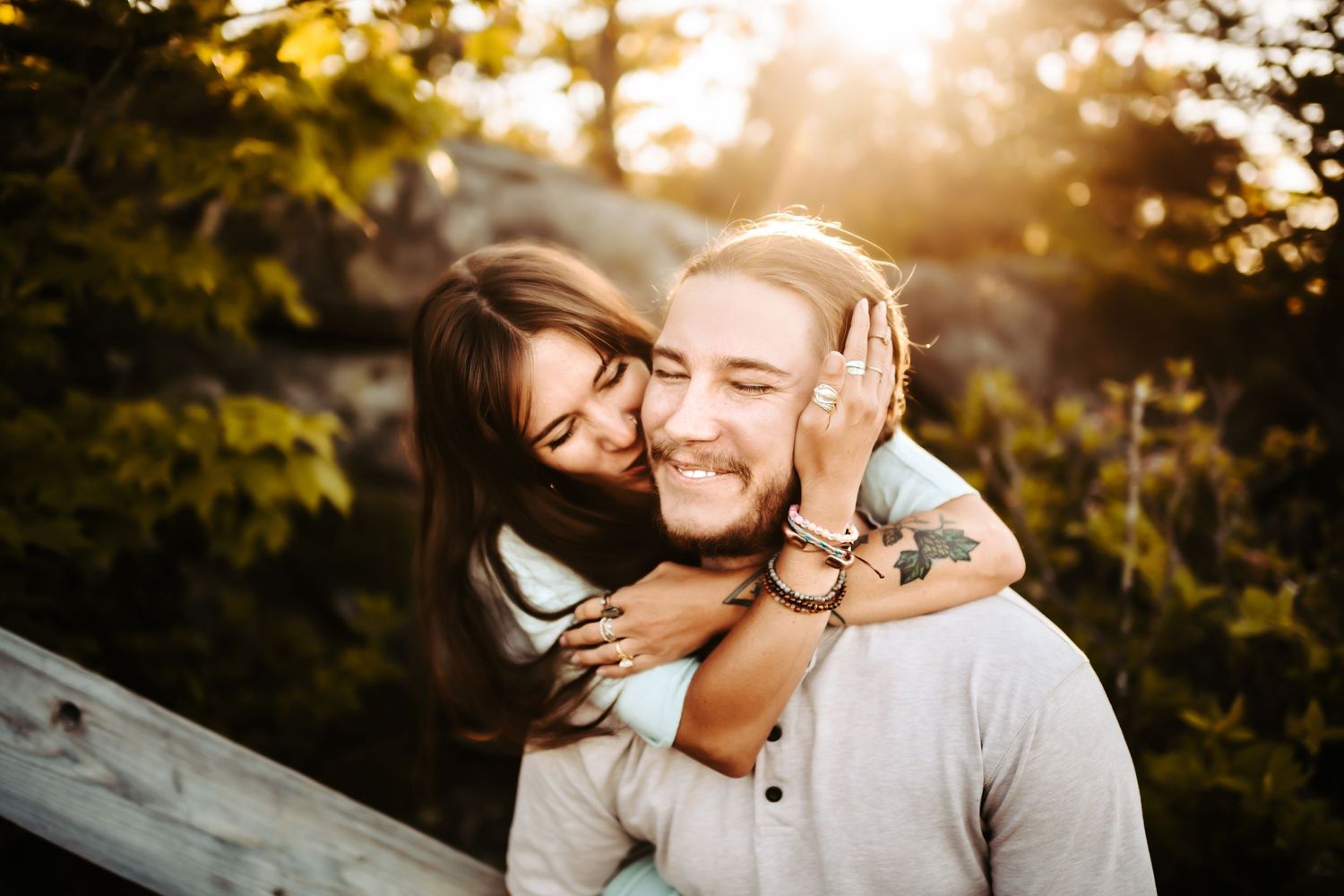 Two people share a tender moment outdoors during golden hour with sunlight filtering through trees.