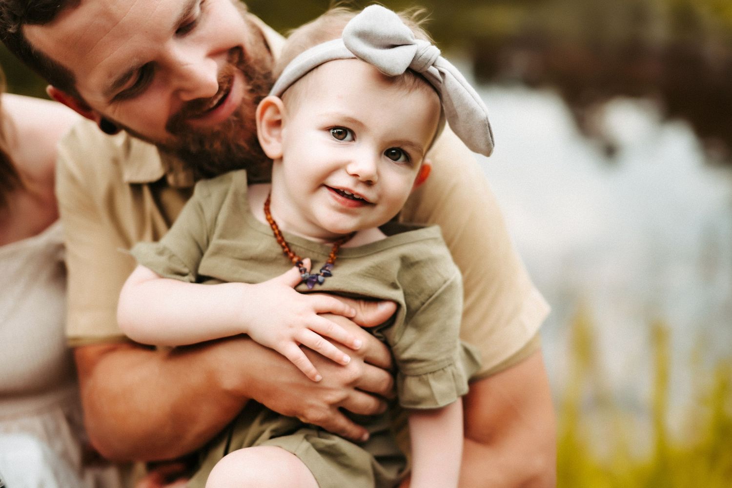 A happy parent and small child sharing a joyful embrace outdoors near a body of water.