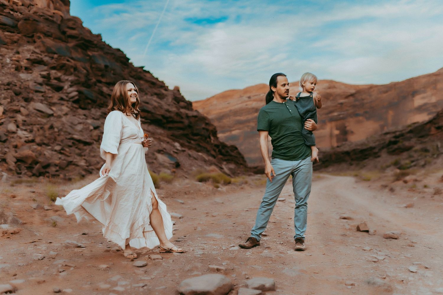 A group of people walking through a scenic desert canyon with red rock formations and blue sky in the background.
