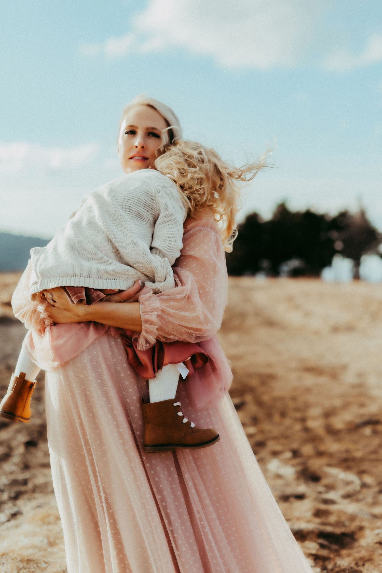 A touching moment captured at sunset on a beach with flowing pink dress and white sweater against a blue sky.