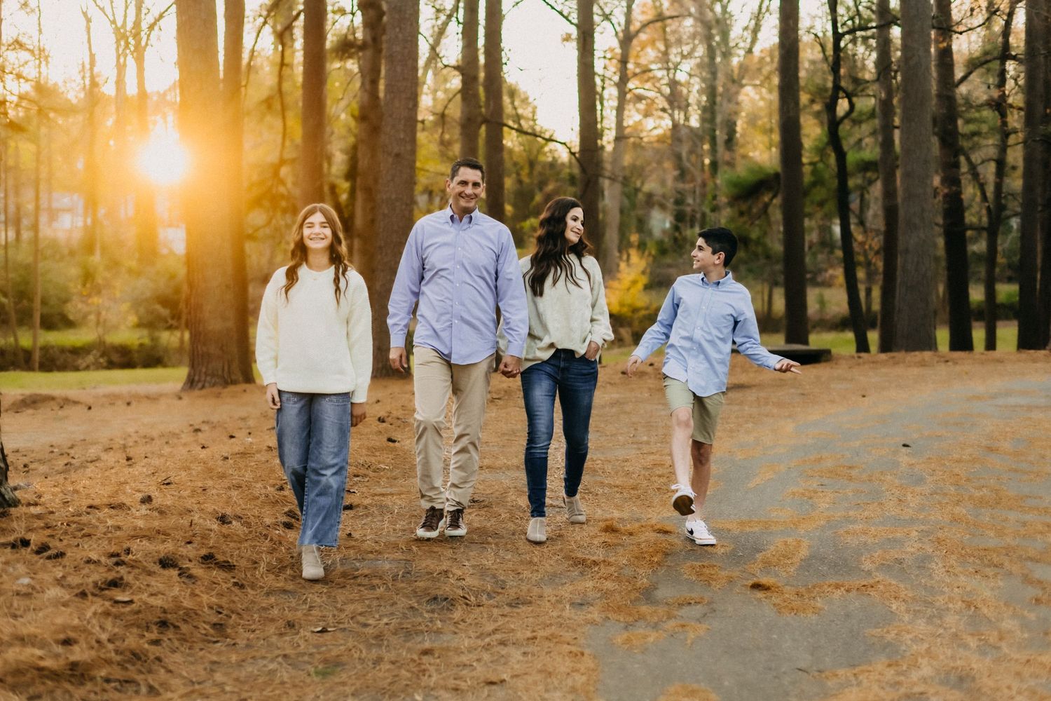 A family takes a stroll together on a dirt path through the woods at sunset with golden sunlight filtering through trees.