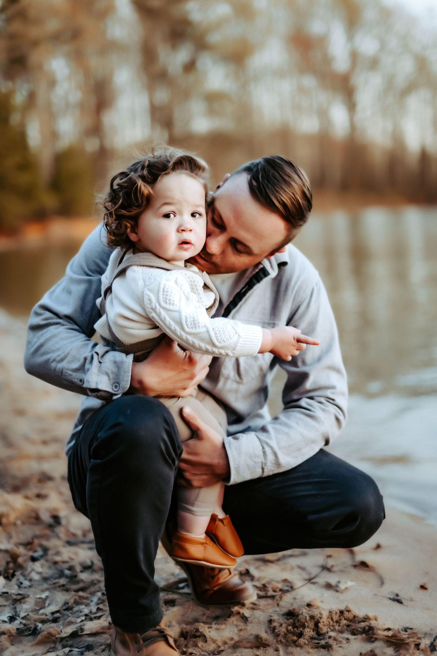 A tender outdoor moment captured by a lake in autumn with fallen leaves on the ground.