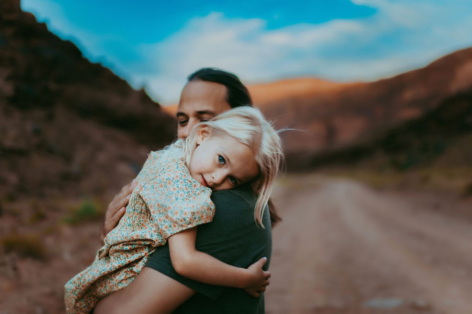 A tender embrace shared on a winding mountain road with golden hills and blue sky in the background.
