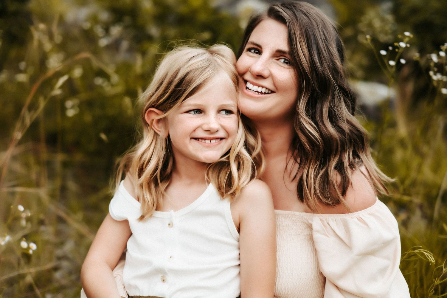 Portrait of two people wearing white tops while sitting outdoors in a natural setting with greenery in the background.