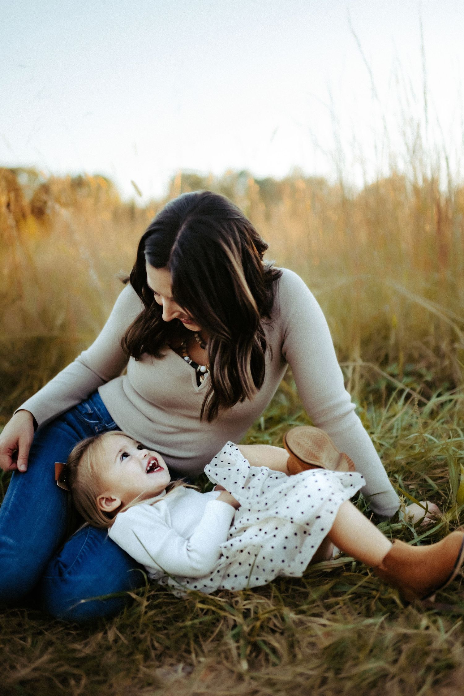 A parent and child share a sweet moment together lying in tall autumn grass during golden hour.