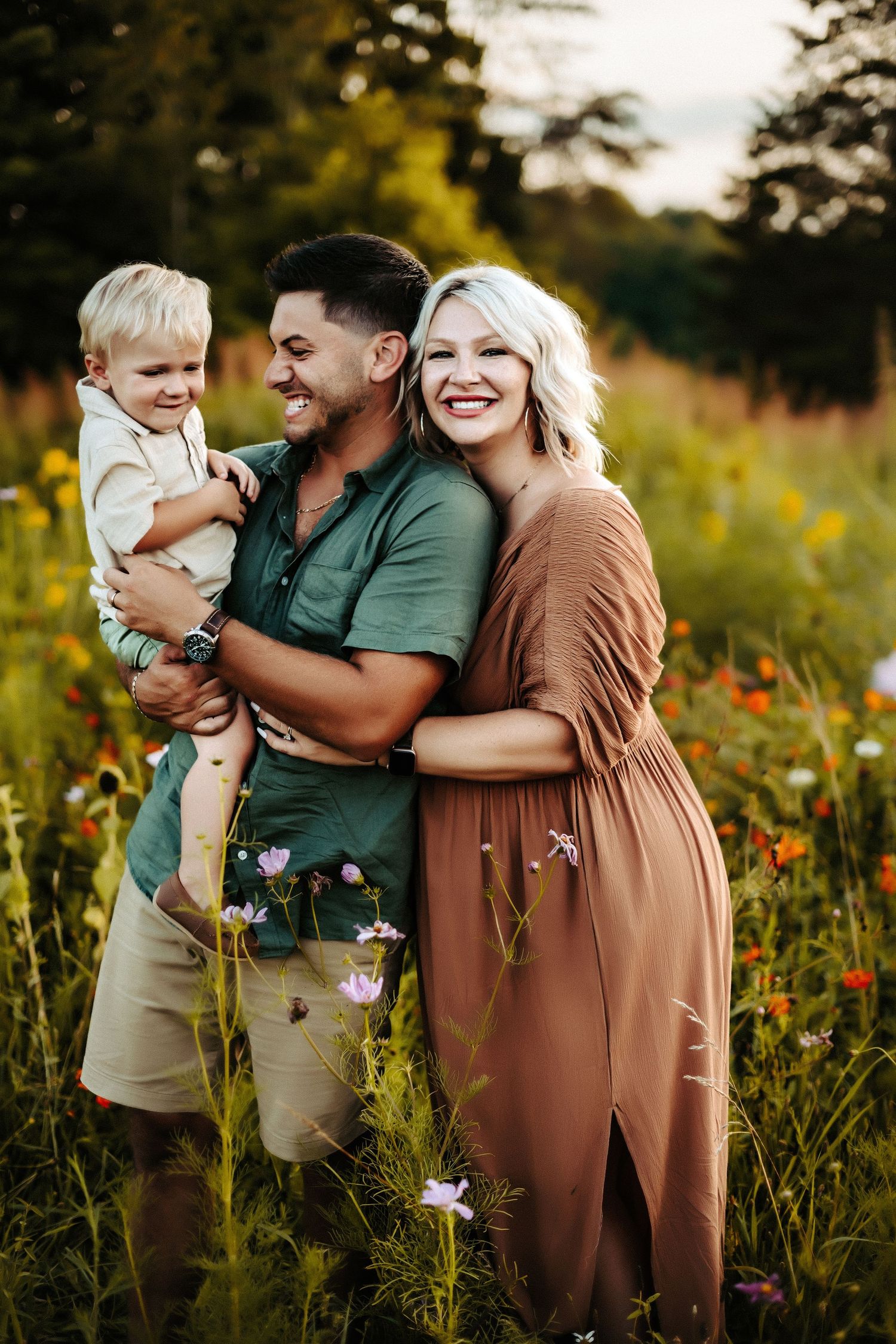 A family poses together in a wildflower meadow at sunset wearing earth-toned clothing among purple and orange blooms.