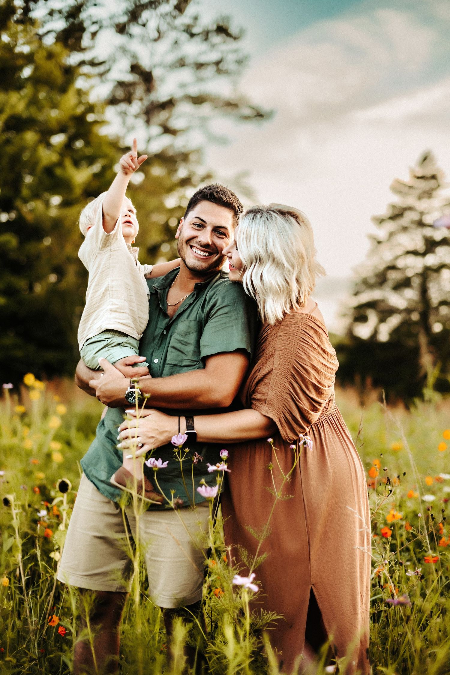 A joyful couple embraces in a wildflower meadow at sunset, surrounded by tall grass and summer blooms.