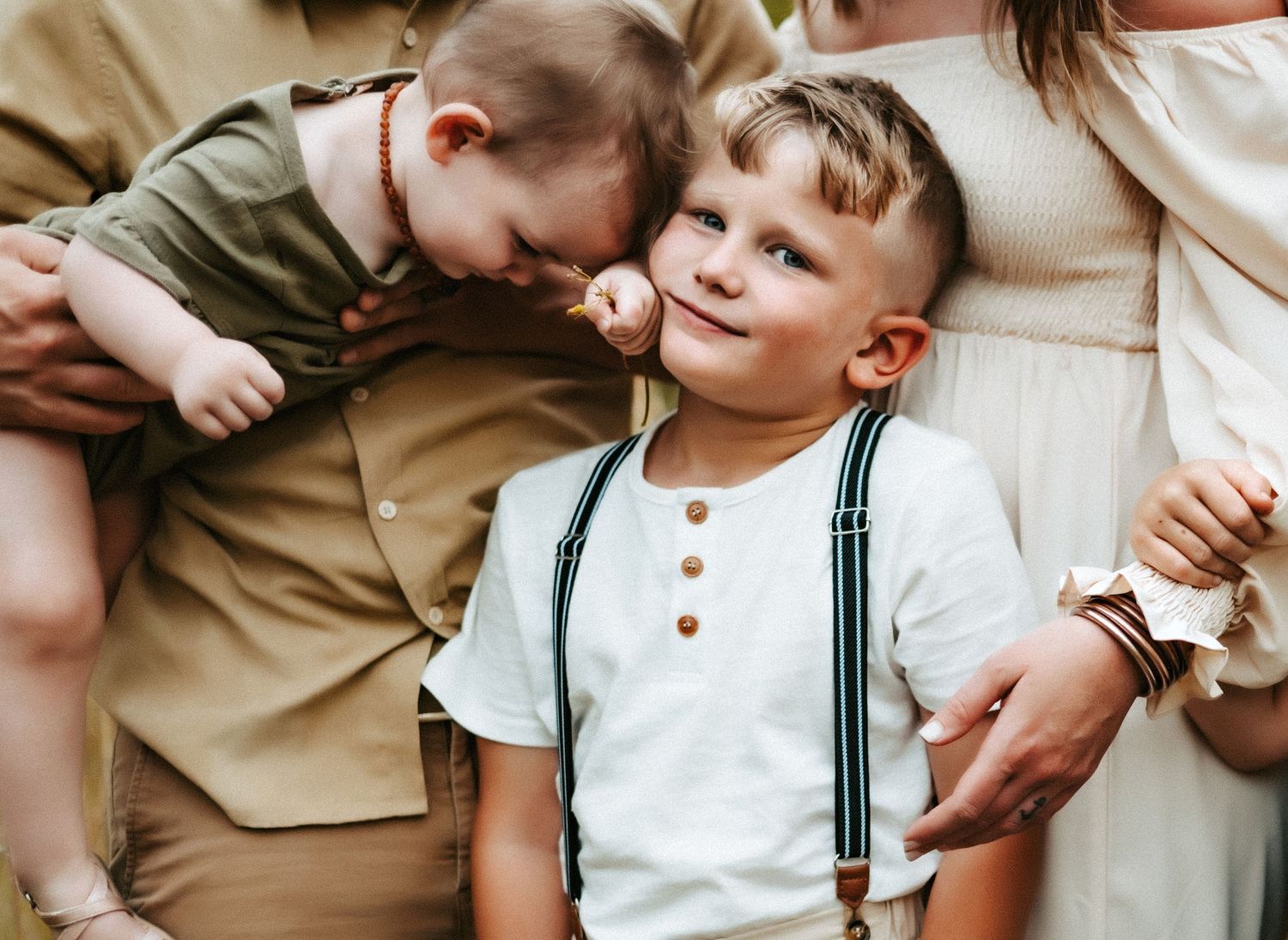 Young children sitting close together on a couch, with one wearing dark suspenders and a white henley shirt.