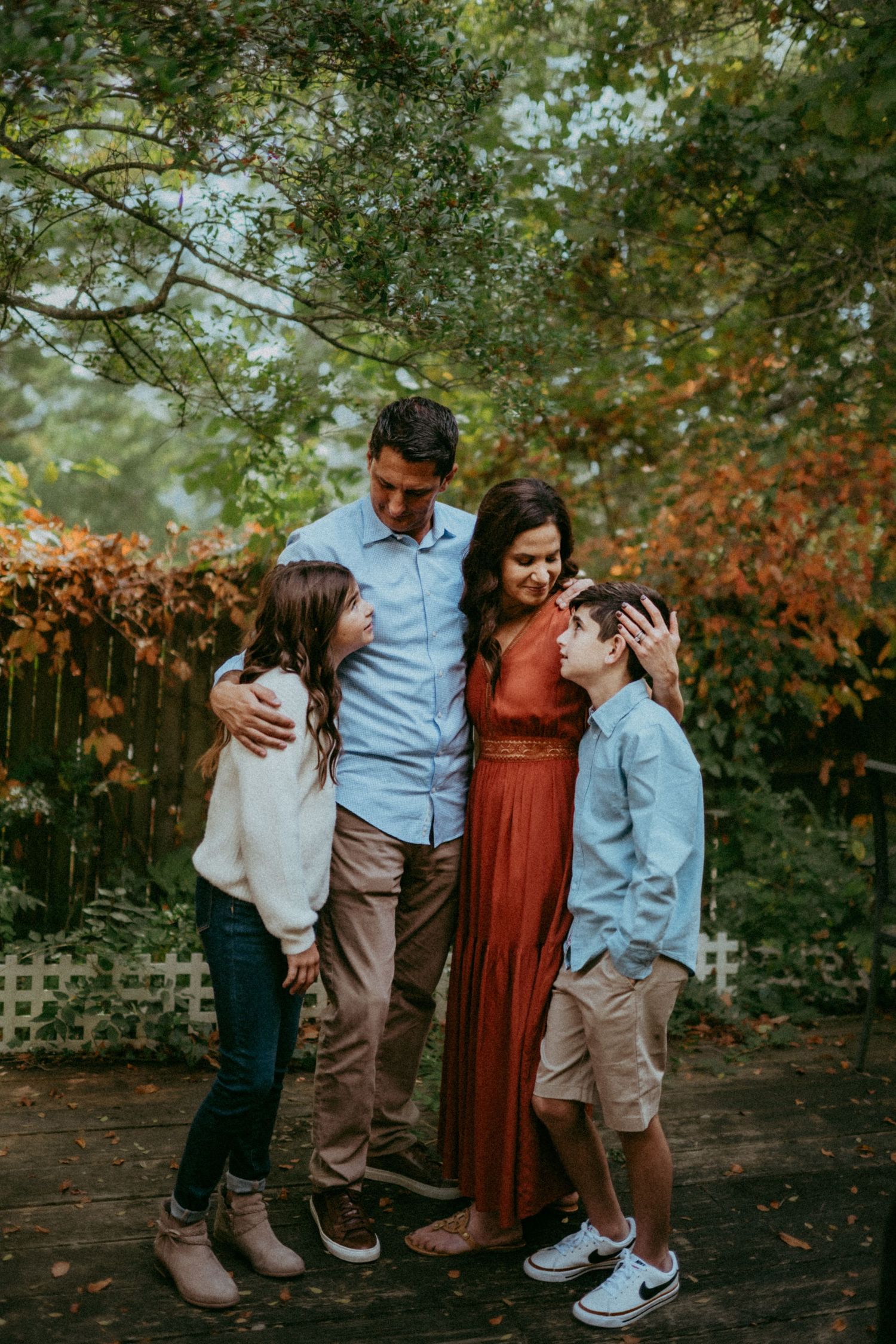 A family of four shares a tender moment together outdoors among autumn foliage in a natural setting.