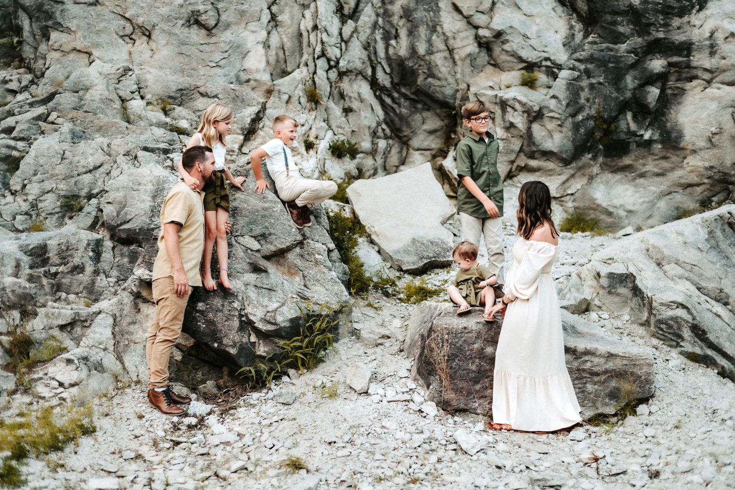 A group in earth-toned clothing poses together on a rocky mountainside terrain against a dramatic stone cliff face.