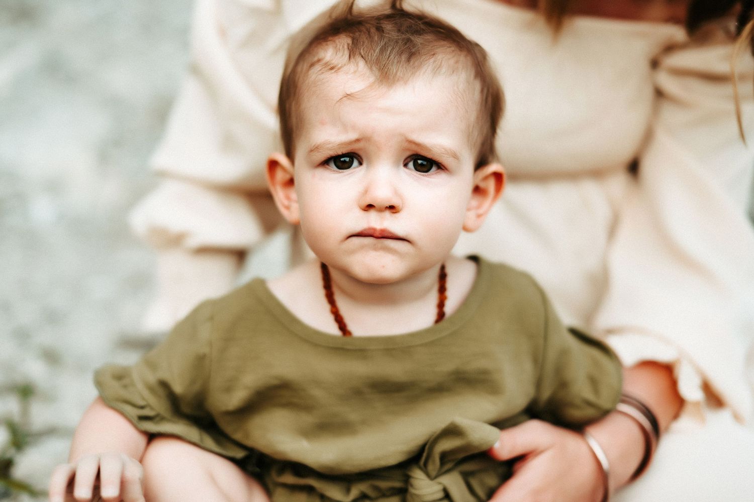 Small child in an olive green shirt sitting with a thoughtful expression.