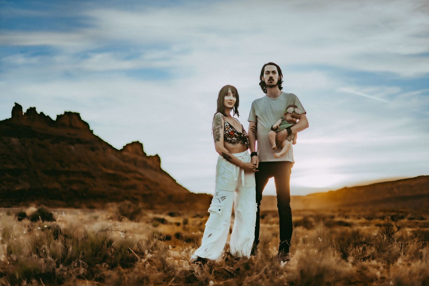 A family stands together in a scenic desert landscape with red rock formations and a warm sunset sky.