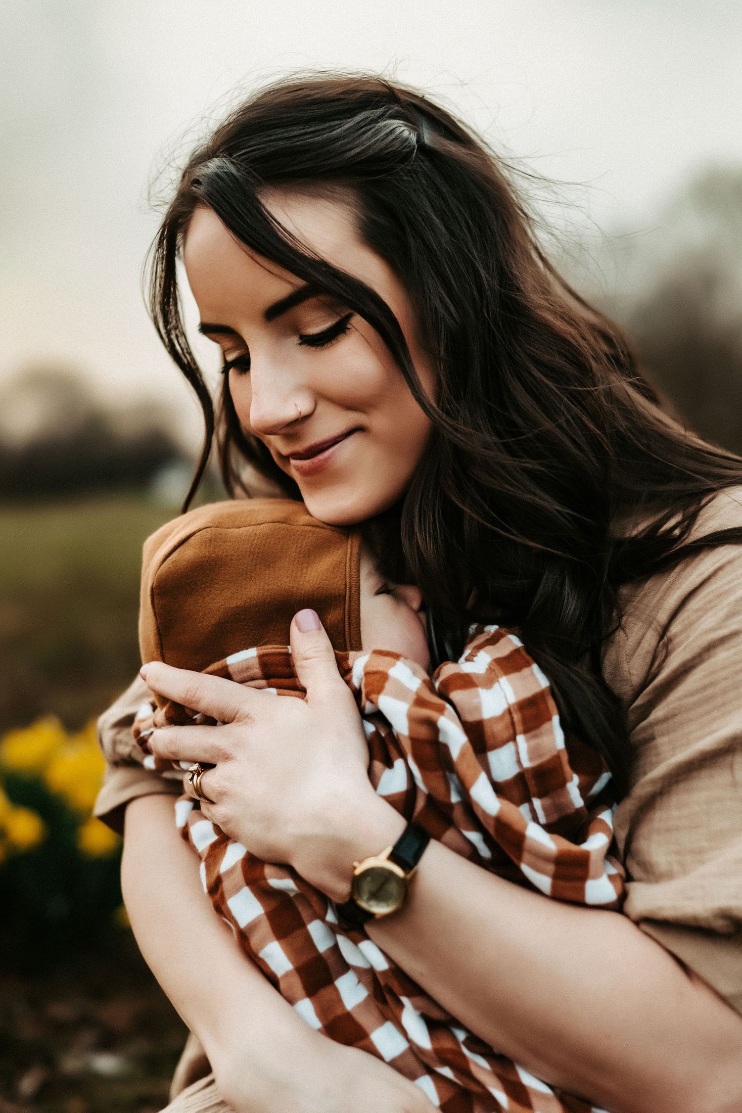 A candid portrait outdoors with dark flowing hair and a brown and white checkered shirt in warm sunlight.