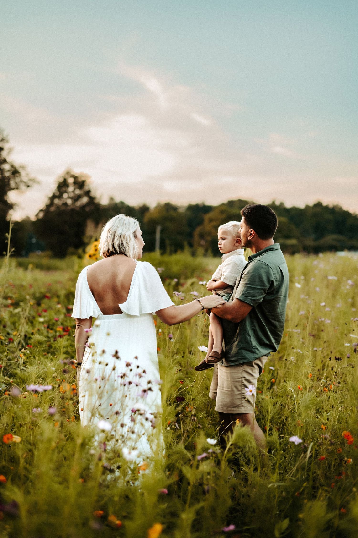 Three people stand together in a summery wildflower meadow at golden hour with trees in the background.