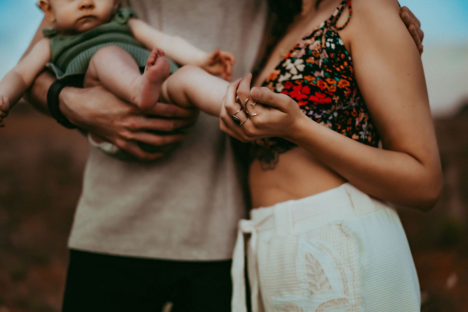 Cropped view of person in floral top holding a baby against blurred outdoor background at sunset.