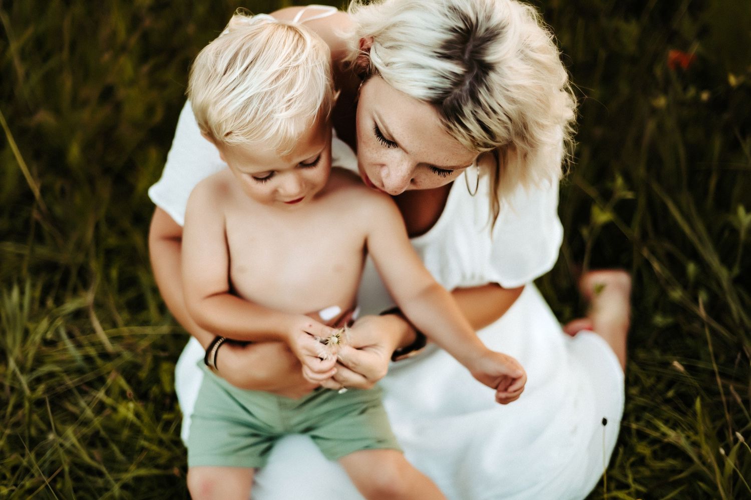 A tender moment shared outdoors in a grassy field on a sunny day wearing white and mint green.