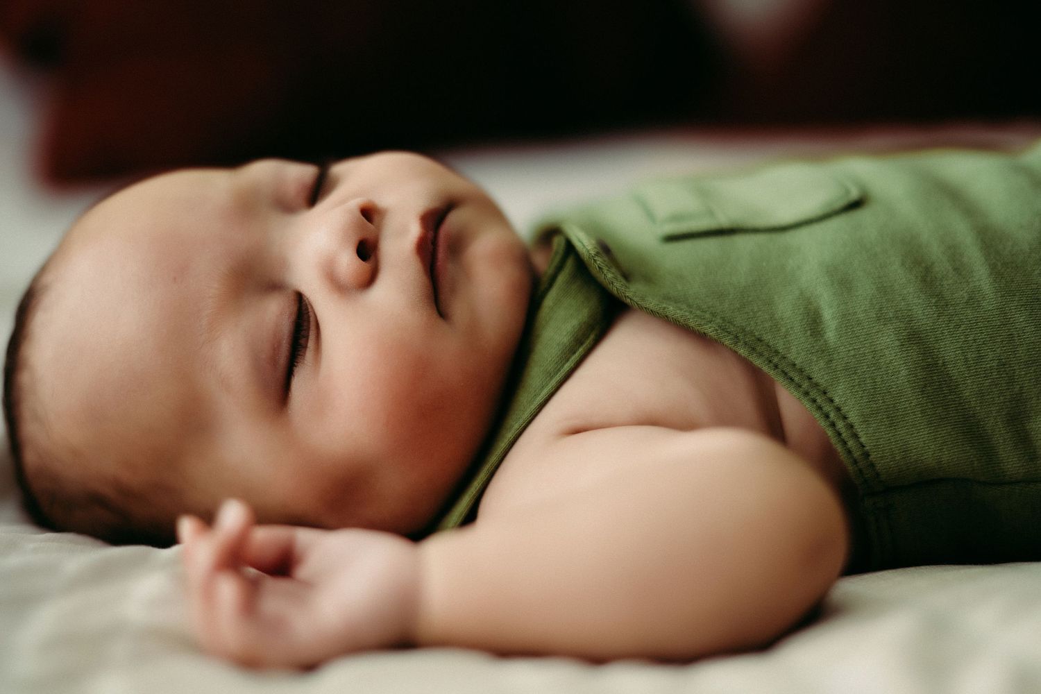 Peaceful baby in a green outfit sleeps soundly on white bedding in soft natural light.