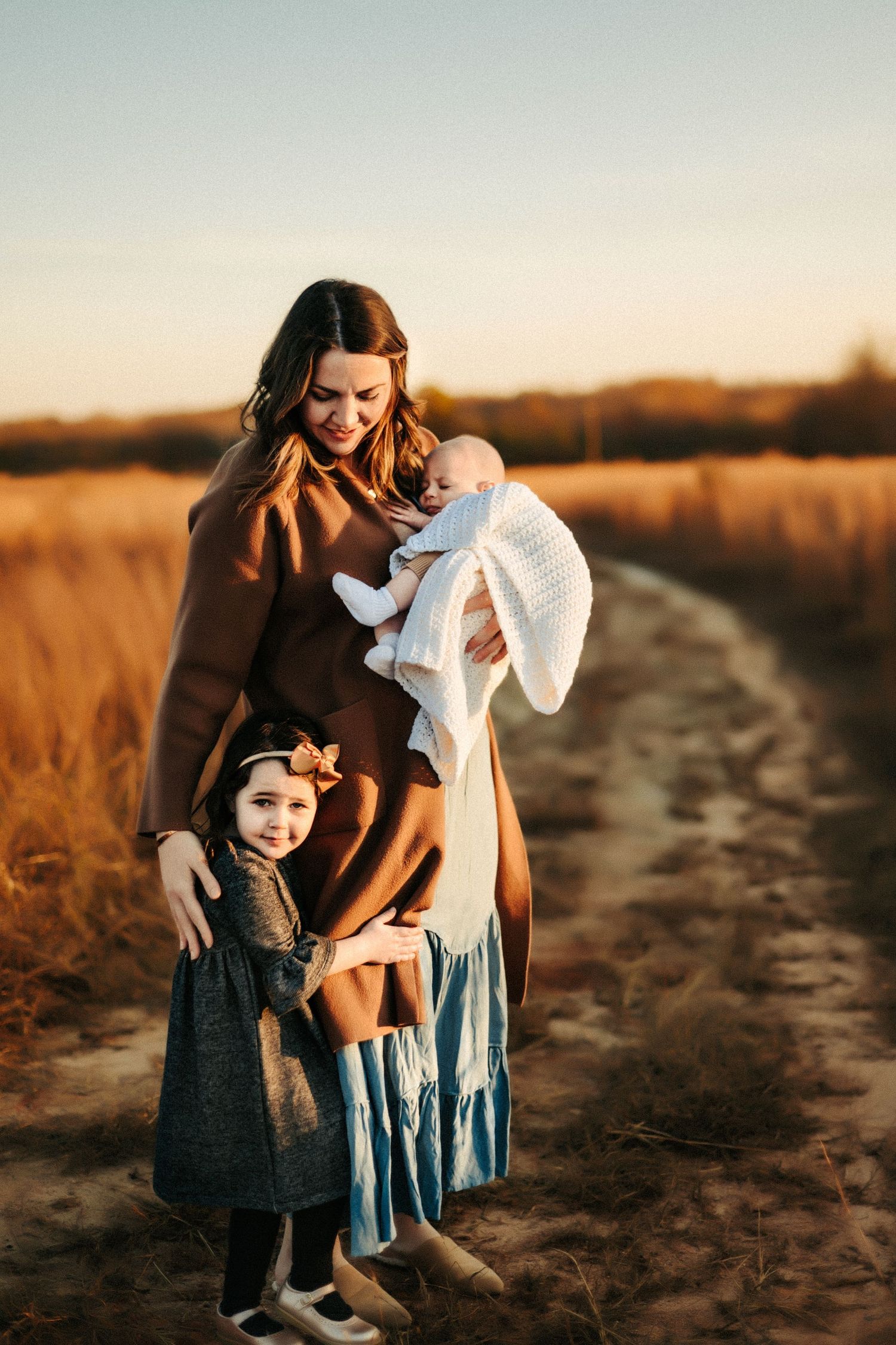 A family stands on a dirt path amidst golden fields at sunset during a warm autumn evening.