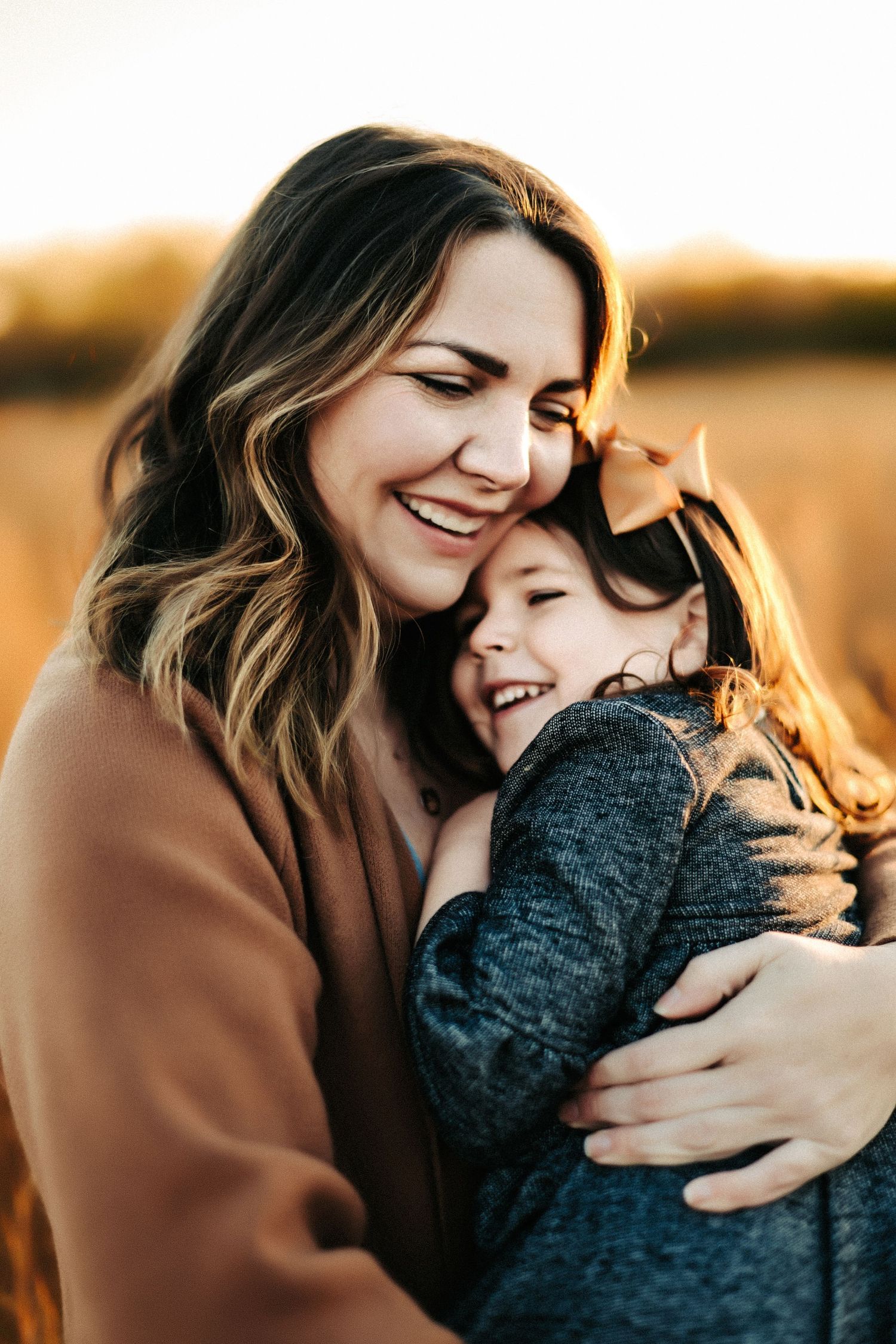 A joyful embrace between parent and child laughing together in warm golden sunlight outdoors.