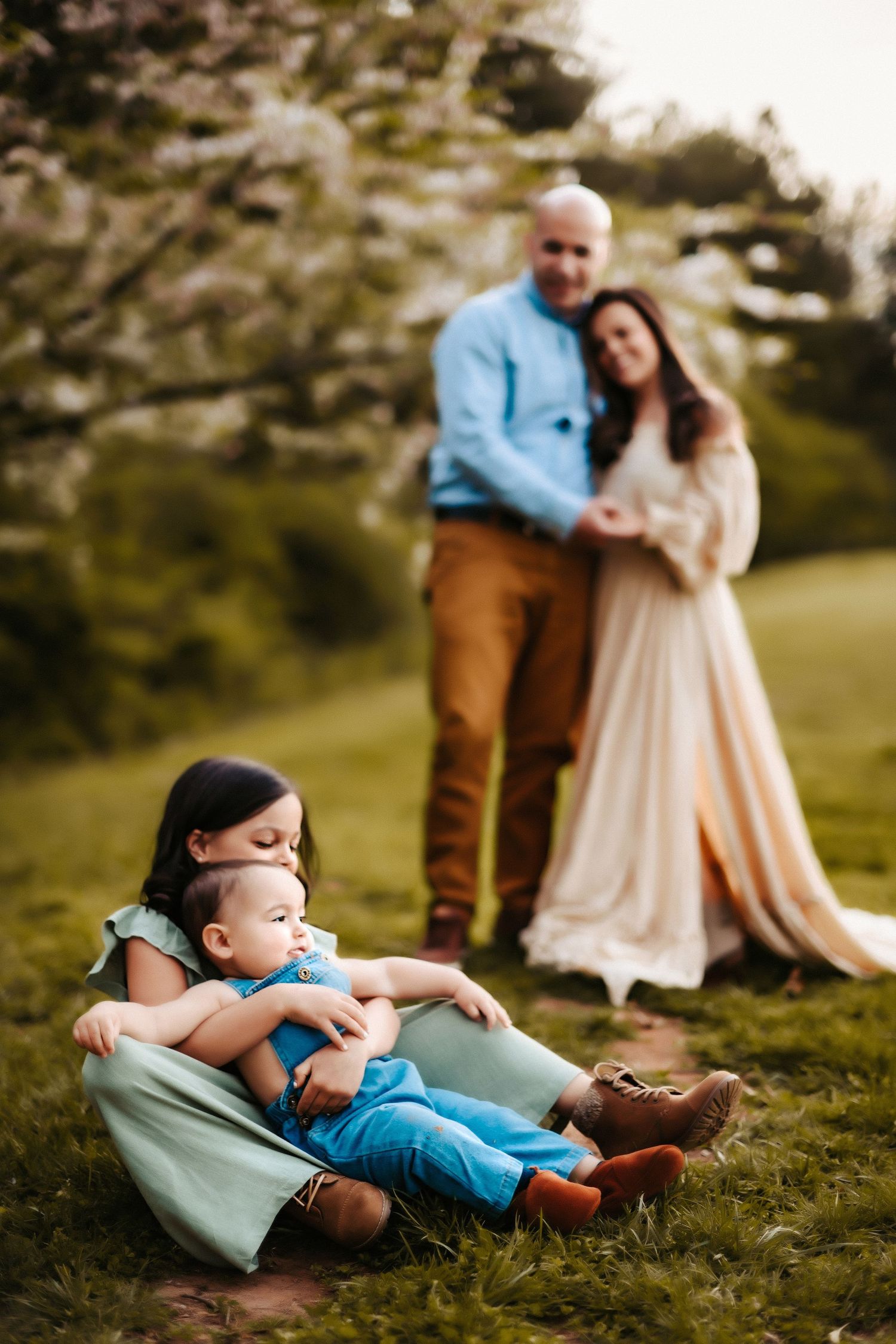 A family poses together on a grassy hillside, with two children sitting in front while adults stand behind them.