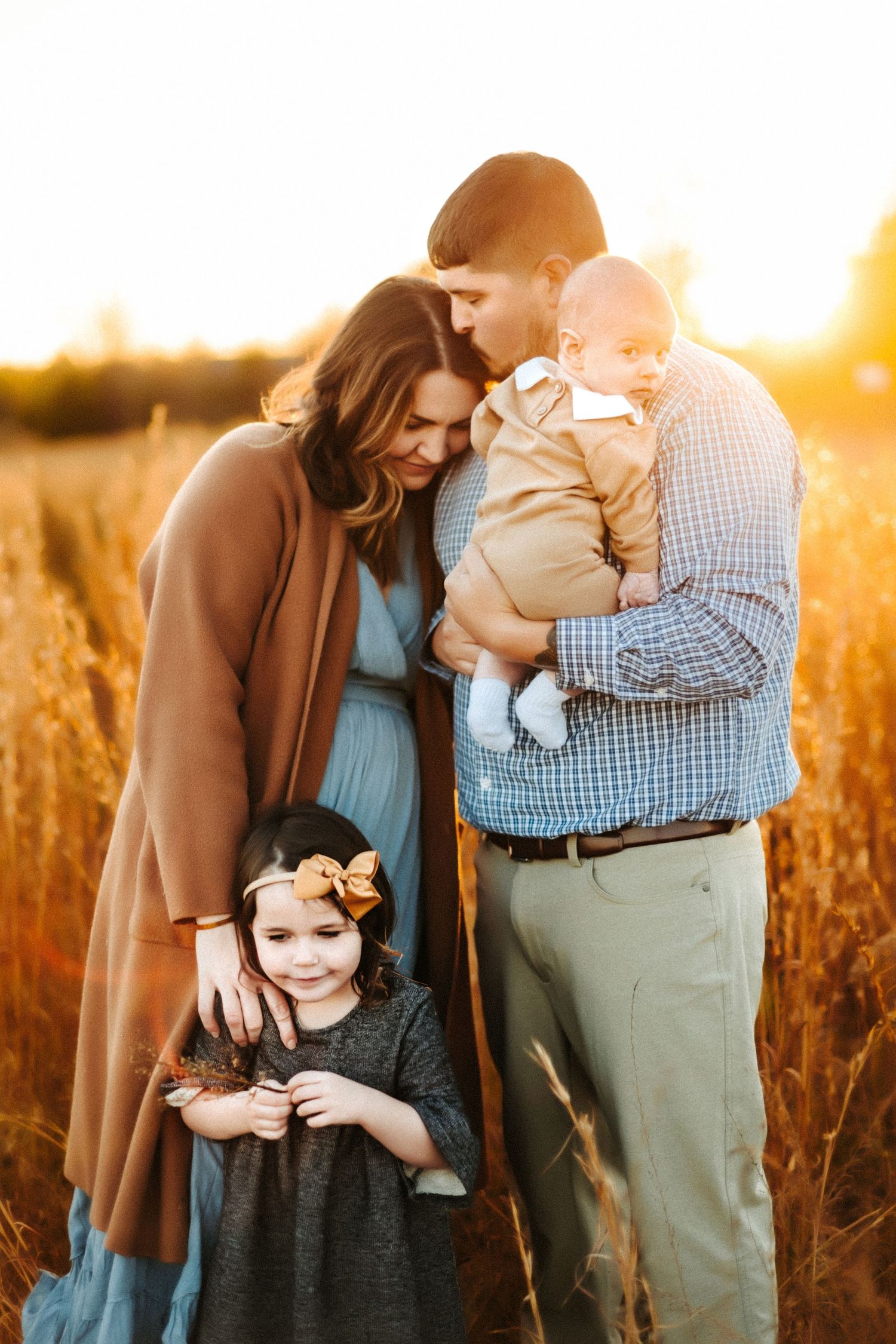 A family shares an intimate moment together in a golden wheat field at sunset.