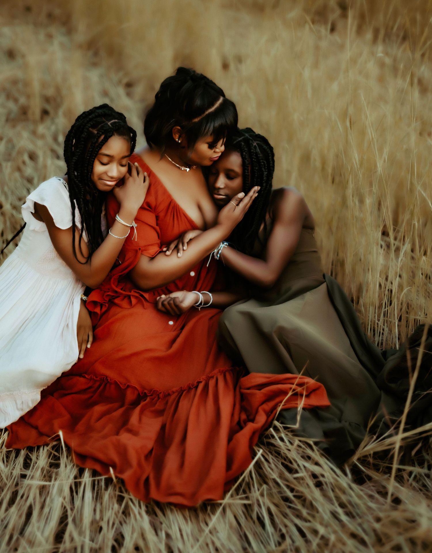A touching portrait of three figures in contrasting dresses sitting close together in a field of golden grass.