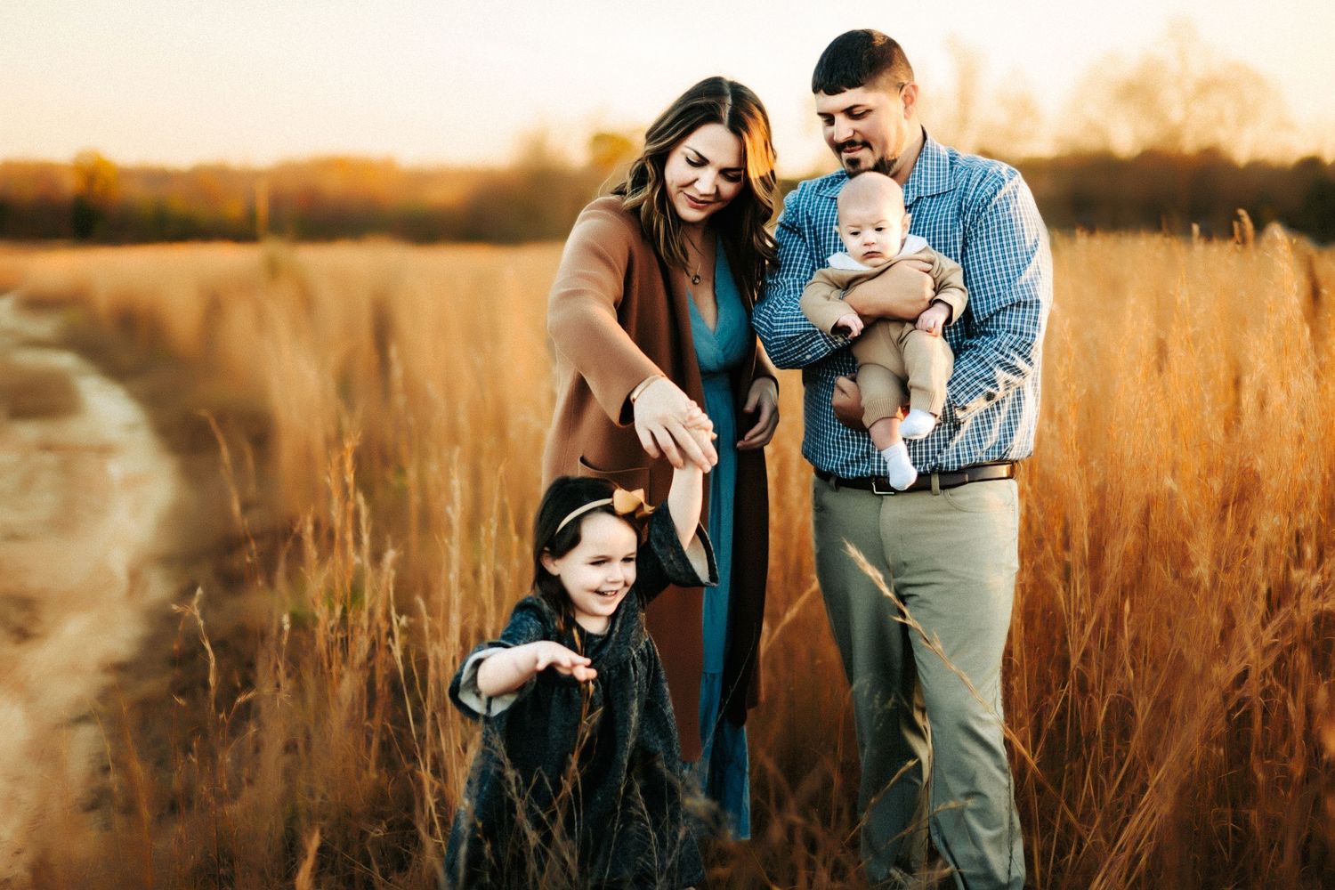 A happy family and their dogs pose together in a golden wheat field at sunset.