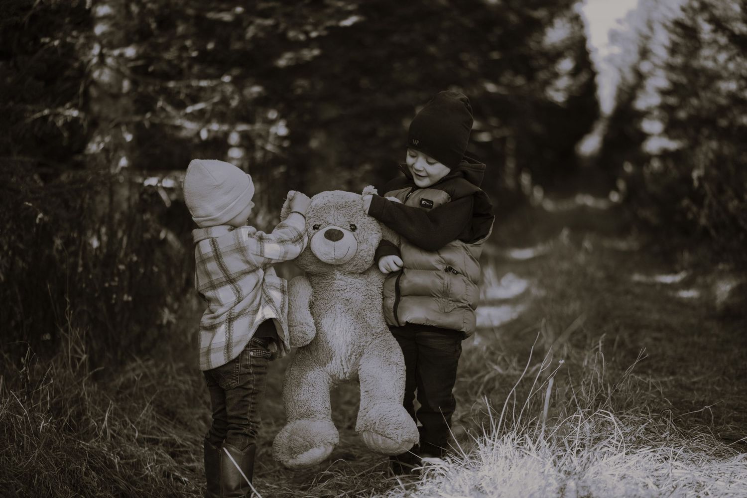 Black and white photo of children walking with a large teddy bear on a forest path.