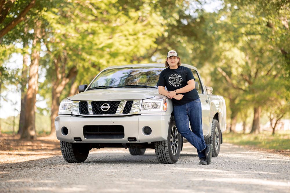 A silver Nissan Titan pickup truck parked on a tree-lined road in natural lighting.