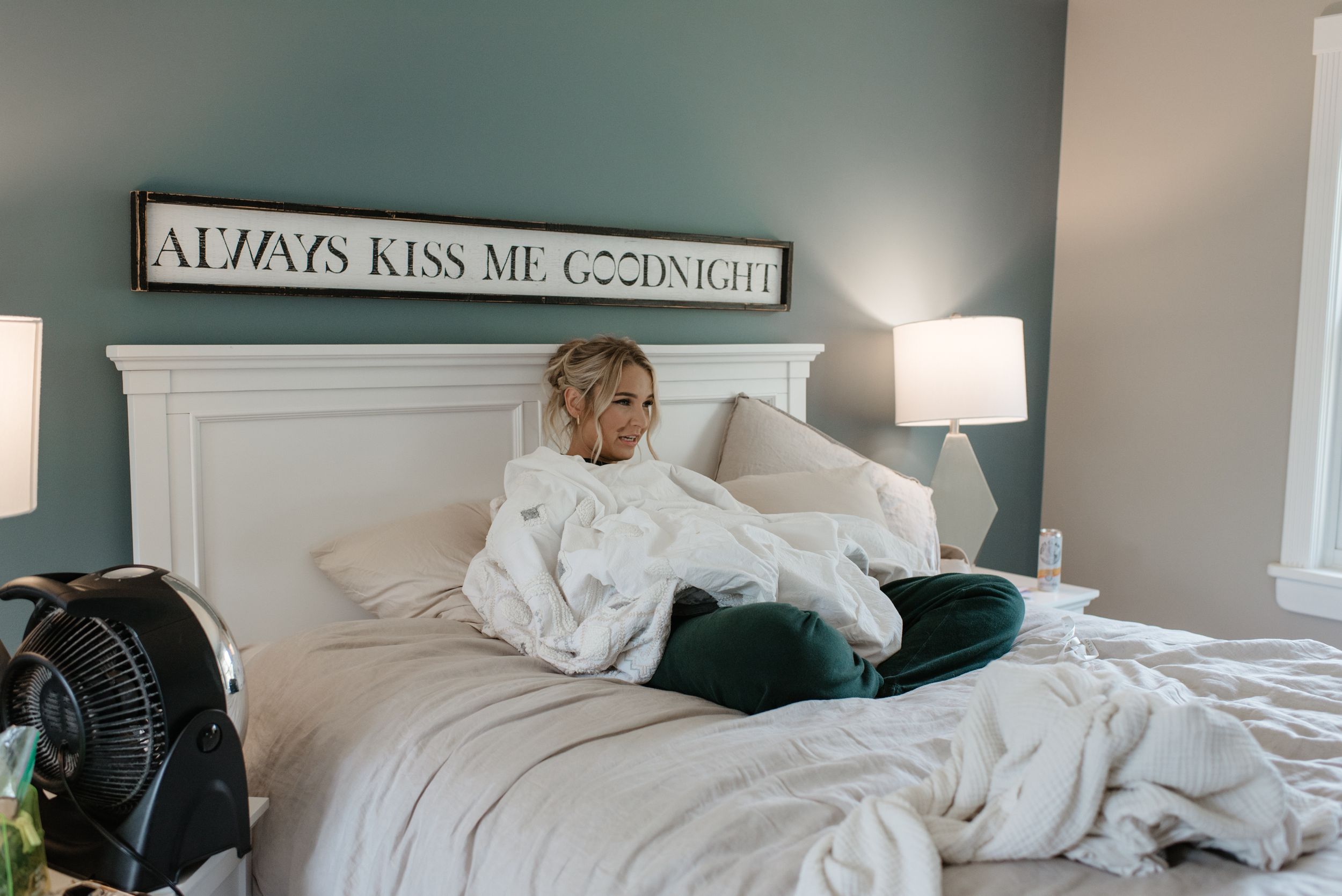 Cozy bedroom interior with white bedding and decorative sign above headboard.