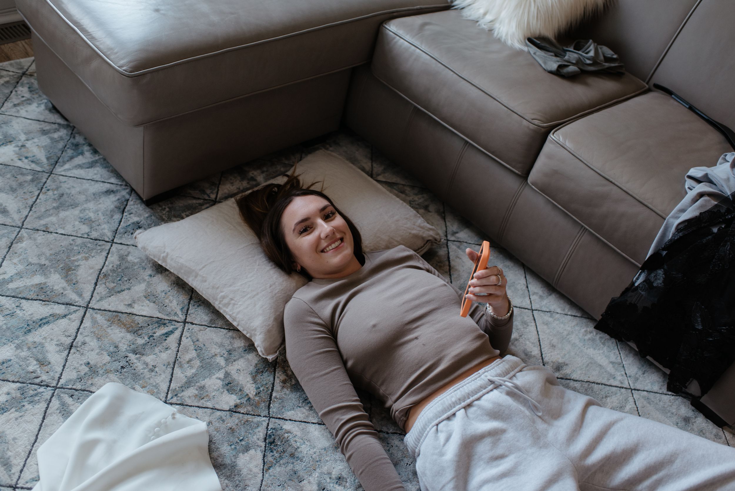 Someone relaxing on floor cushions beside a gray couch while holding a water bottle.