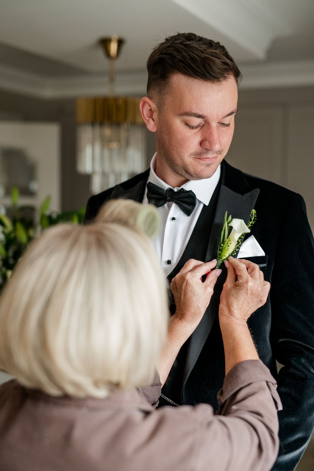 A boutonniere is being pinned to a black tuxedo lapel during a formal event preparation.