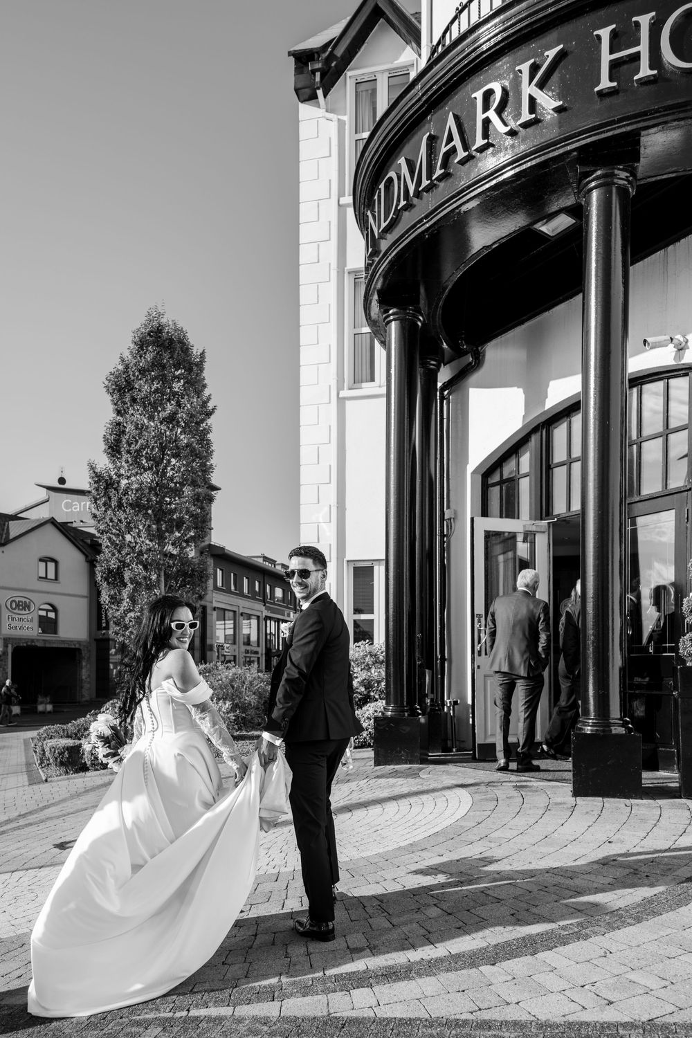 A couple in wedding attire share a romantic moment outside a hotel entrance in black and white photography.