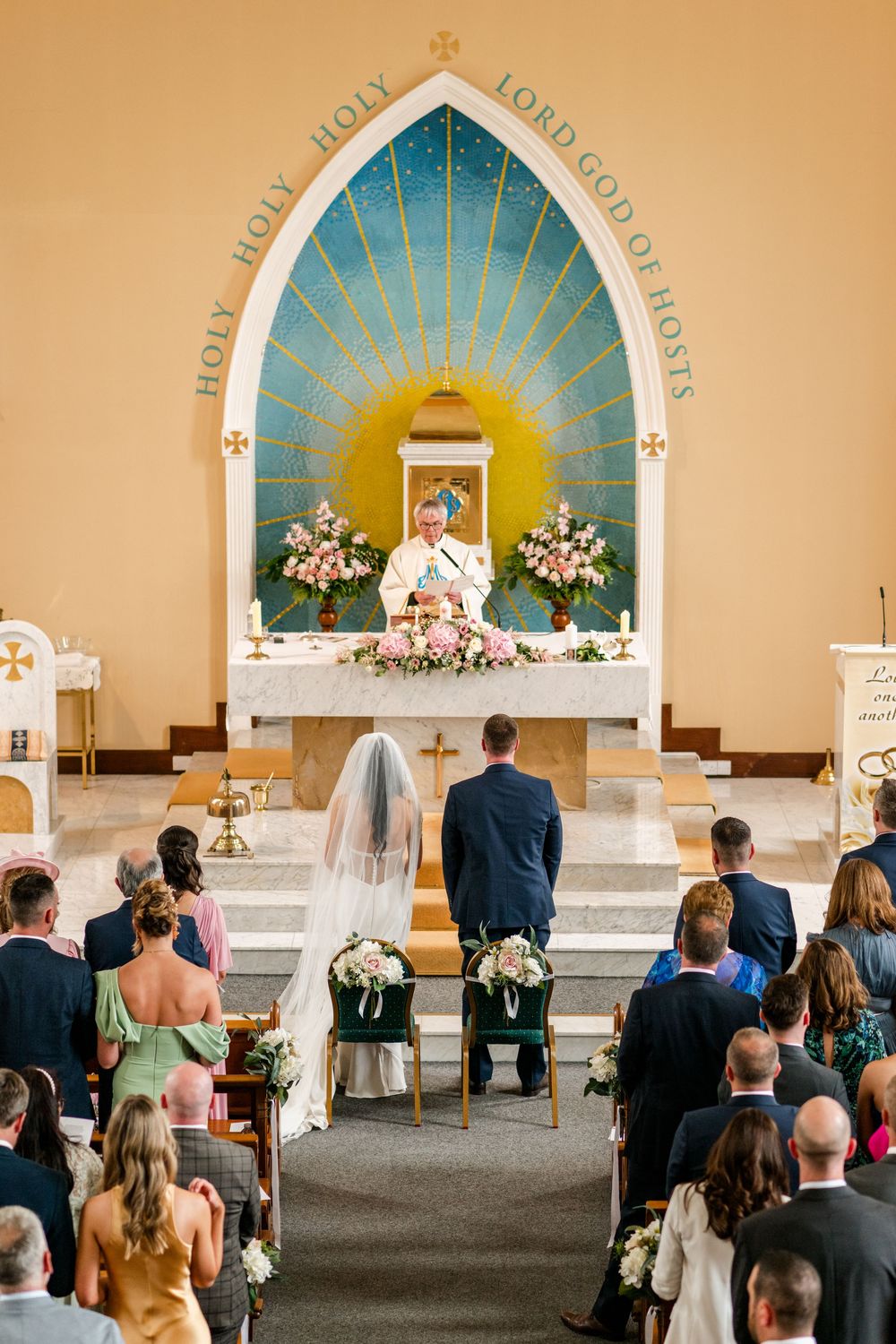 Church wedding ceremony in progress with guests seated in pews and decorative floral arrangements at the altar.