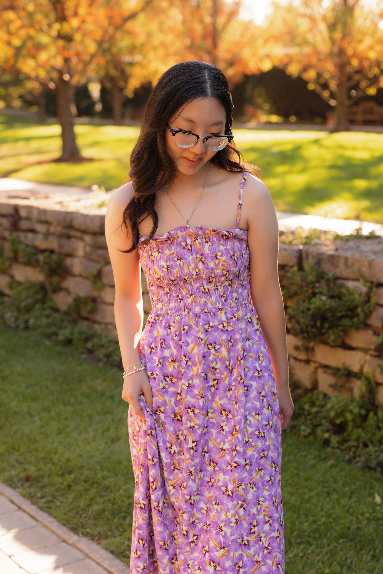 Person wearing purple floral maxi dress standing in garden during golden hour.