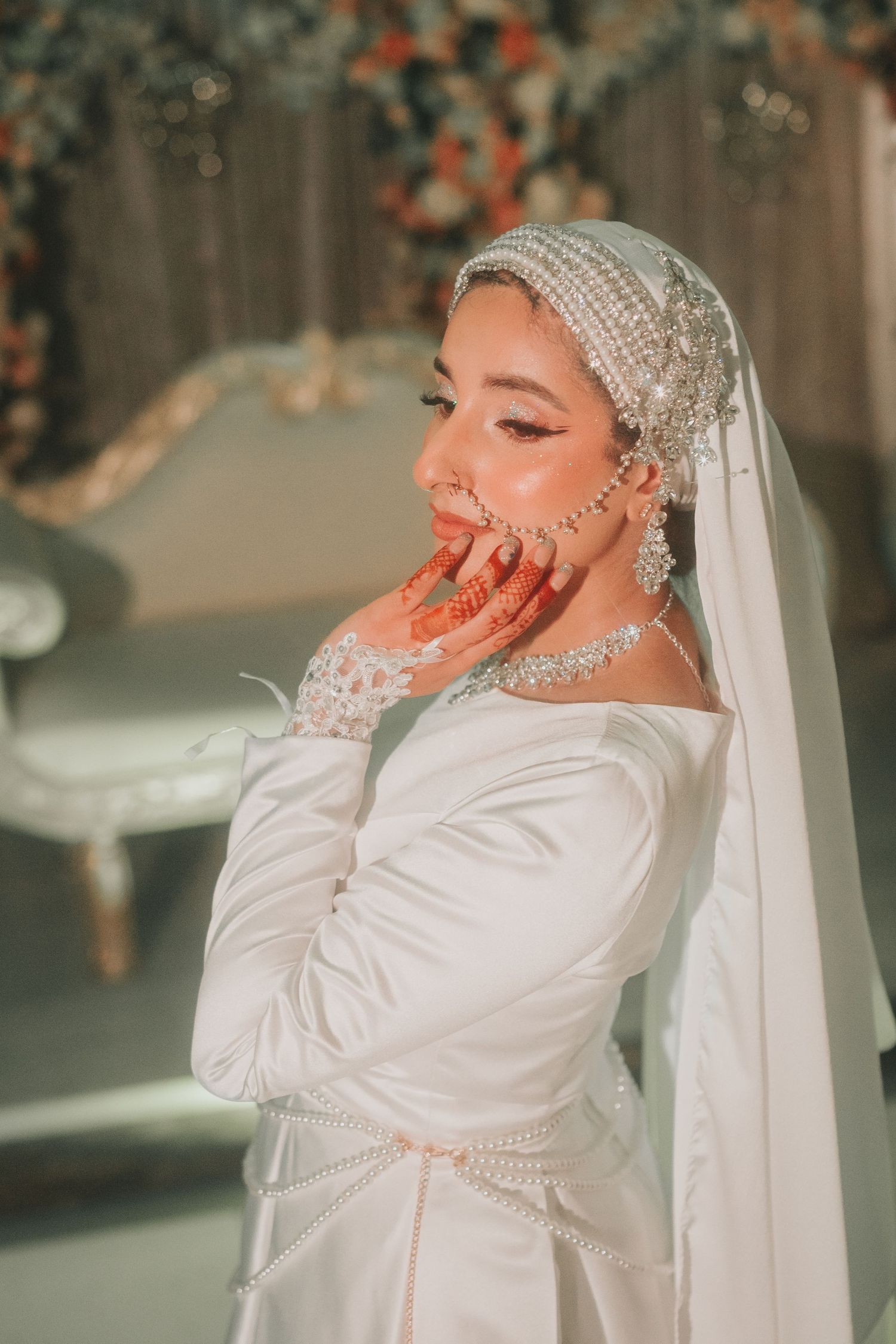 Bride in elegant white dress and pearl headpiece poses with graceful hand gesture.
