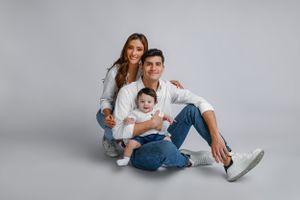Family wearing denim and white outfits pose together on light gray studio background.