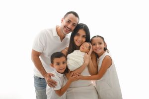 A smiling family dressed in white poses together against a soft white background for a studio portrait.
