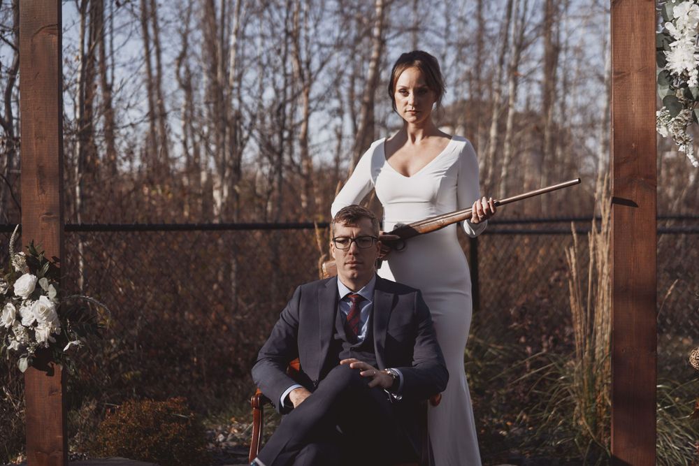 A couple dressed in elegant attire poses together in a rustic outdoor forest setting at dusk.