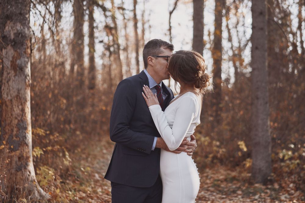 A couple in wedding attire share a tender embrace in an autumnal forest setting during golden hour.