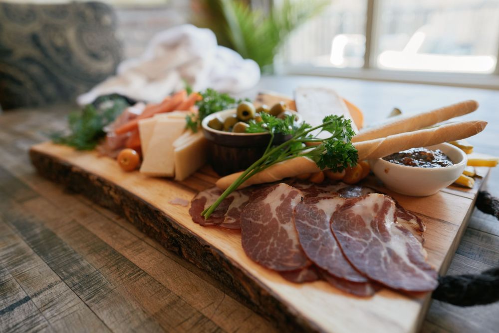 Rustic charcuterie board with sliced meats, cheese, broccoli and dipping sauces served on a wooden plank.