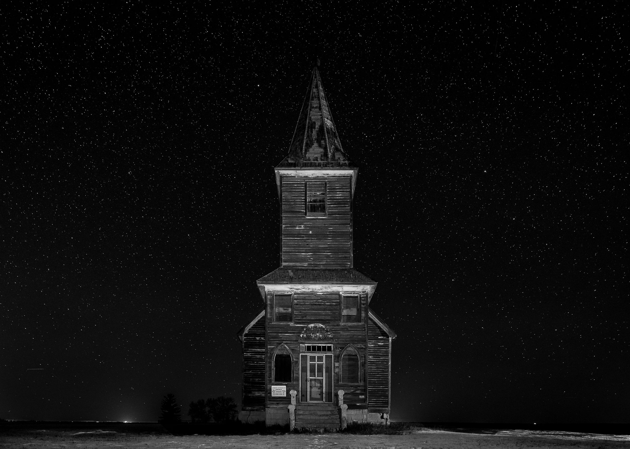 An abandoned wooden church stands isolated against a stark black and white winter landscape.