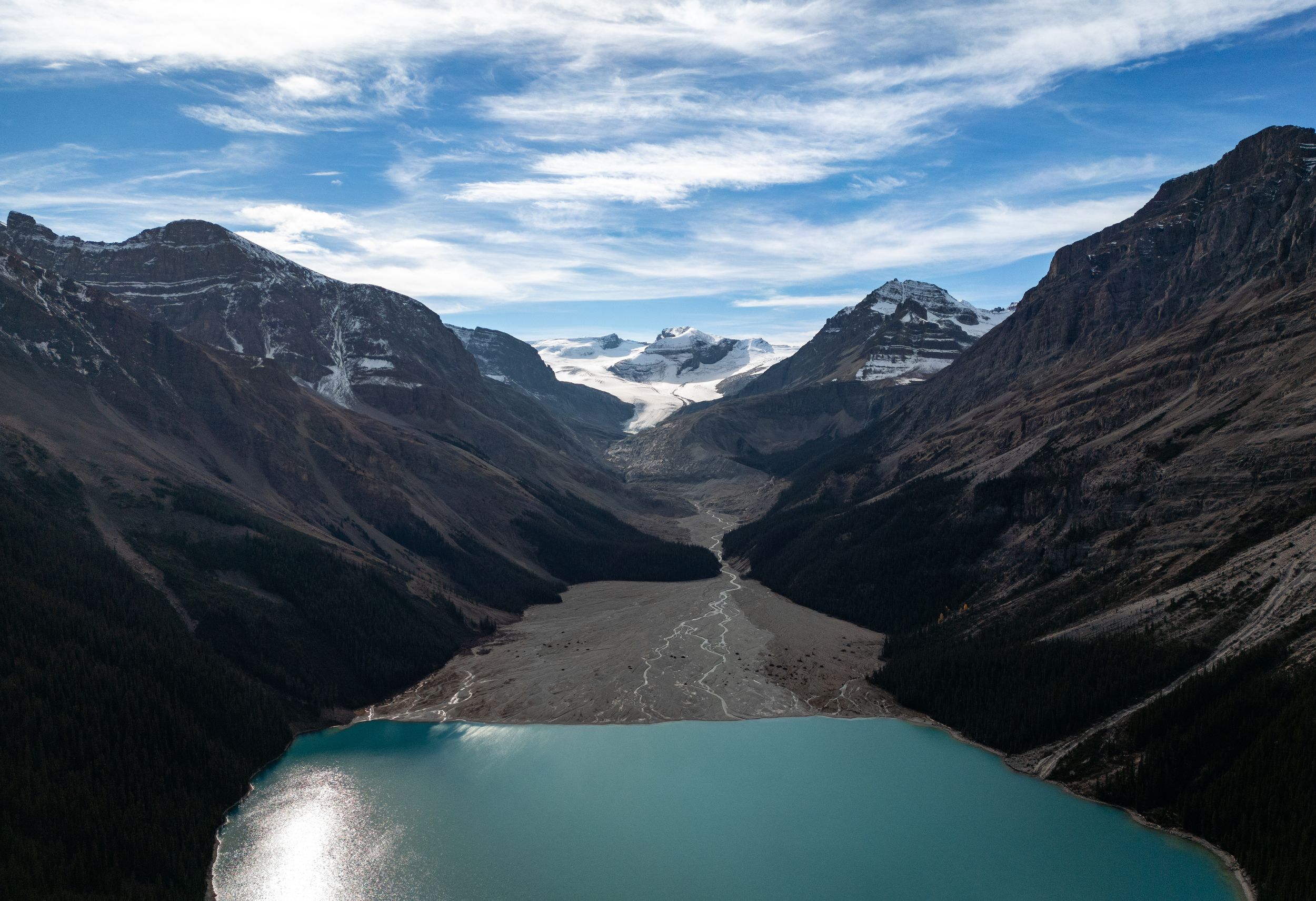 Panoramic view of snow-capped mountain peaks and turquoise glacial lake under dramatic cloudy skies in Banff National Park.