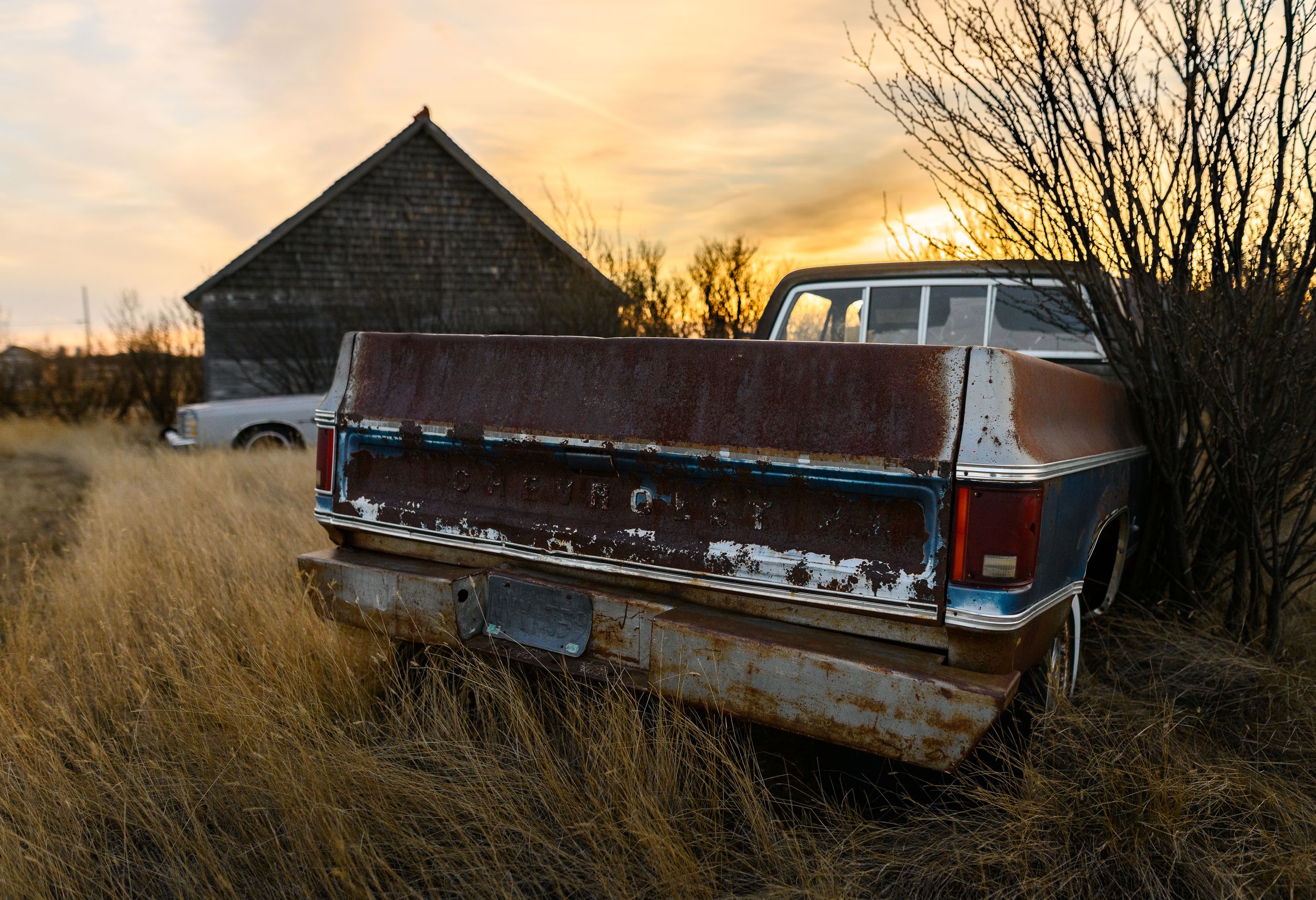 Rustic barn and vintage pickup truck silhouetted against a golden sunset in tall grass.