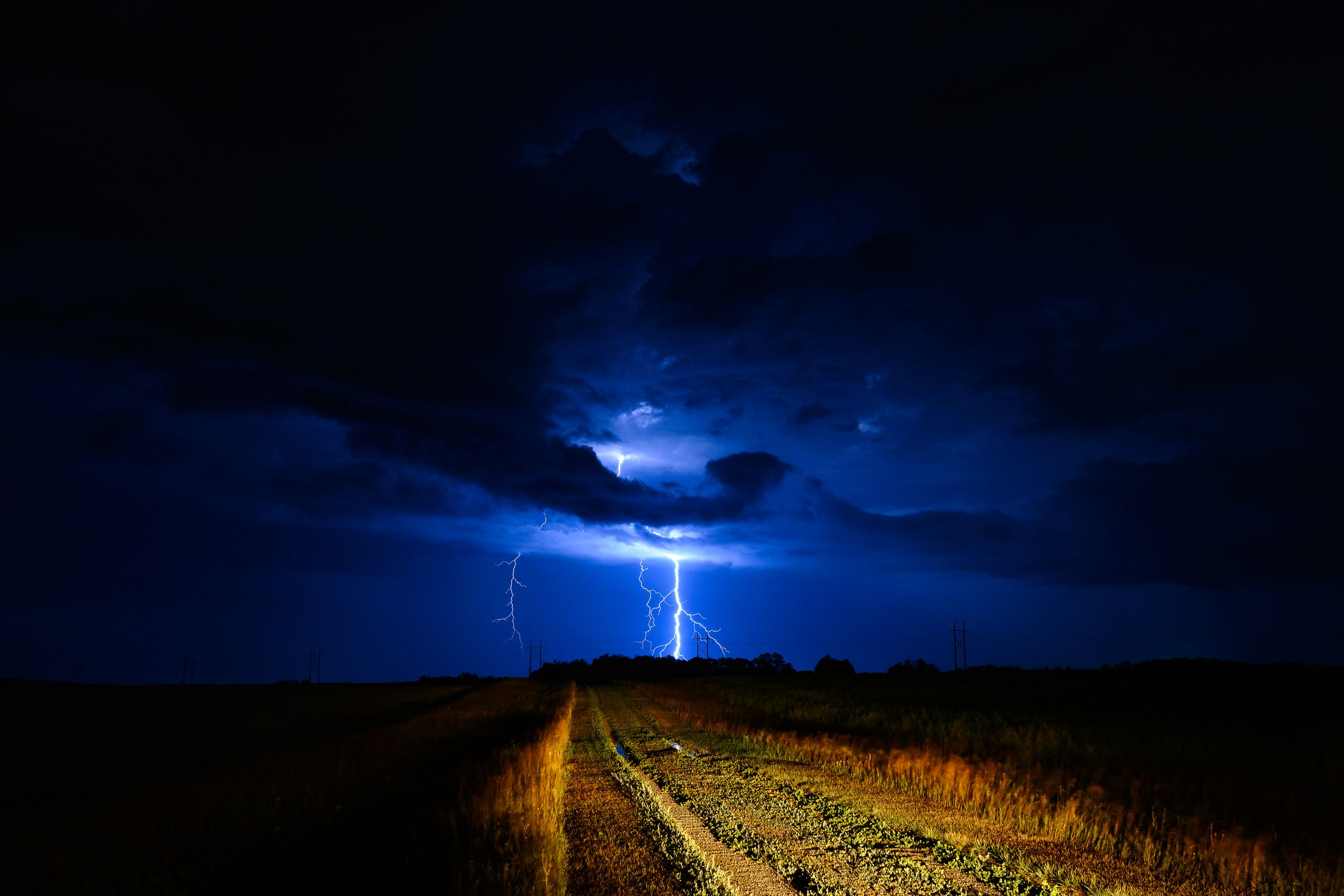 Lightning strike illuminates a rural dirt road against a dark stormy night sky.