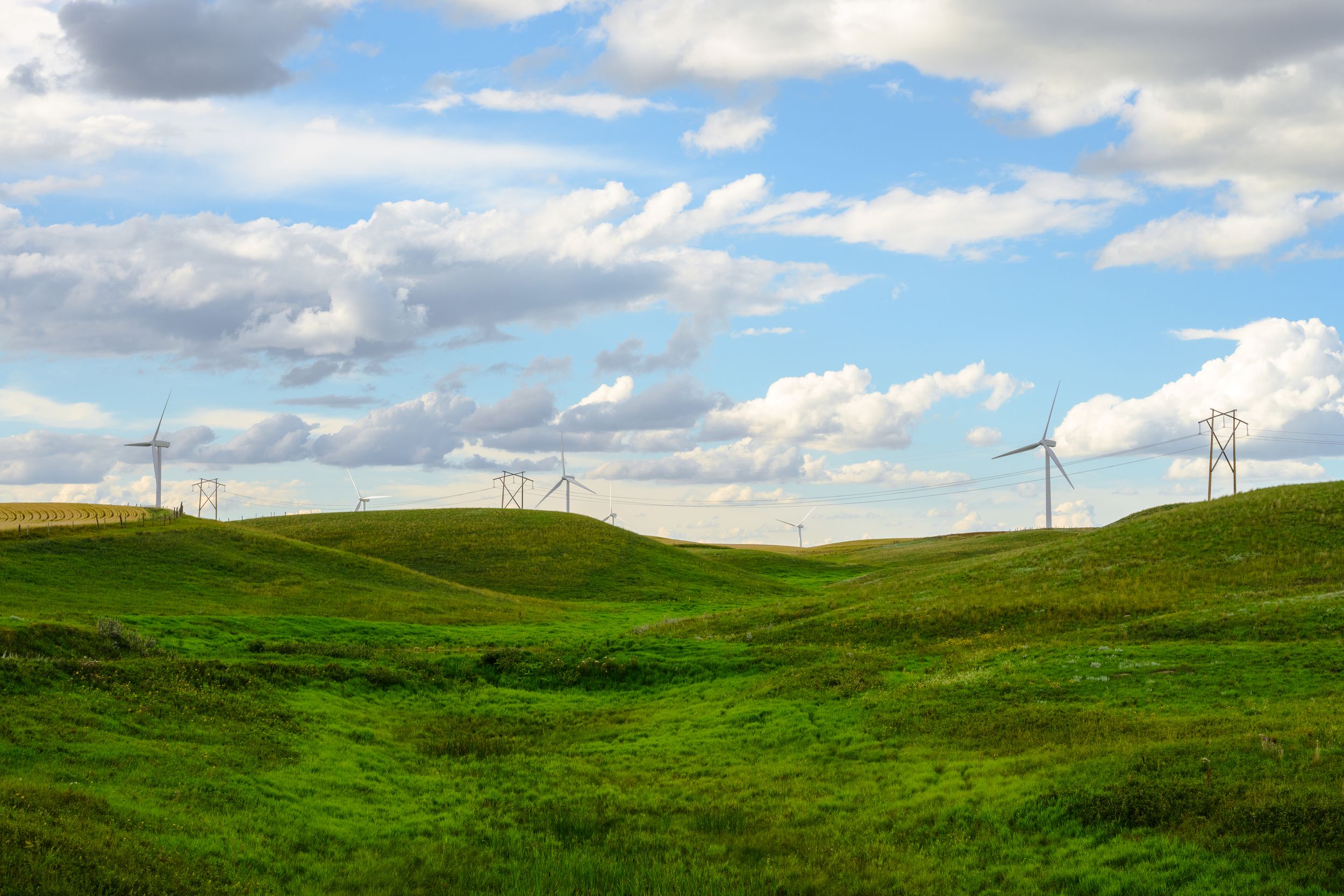 Rolling green hills stretch across the landscape under a bright blue sky dotted with puffy white clouds.