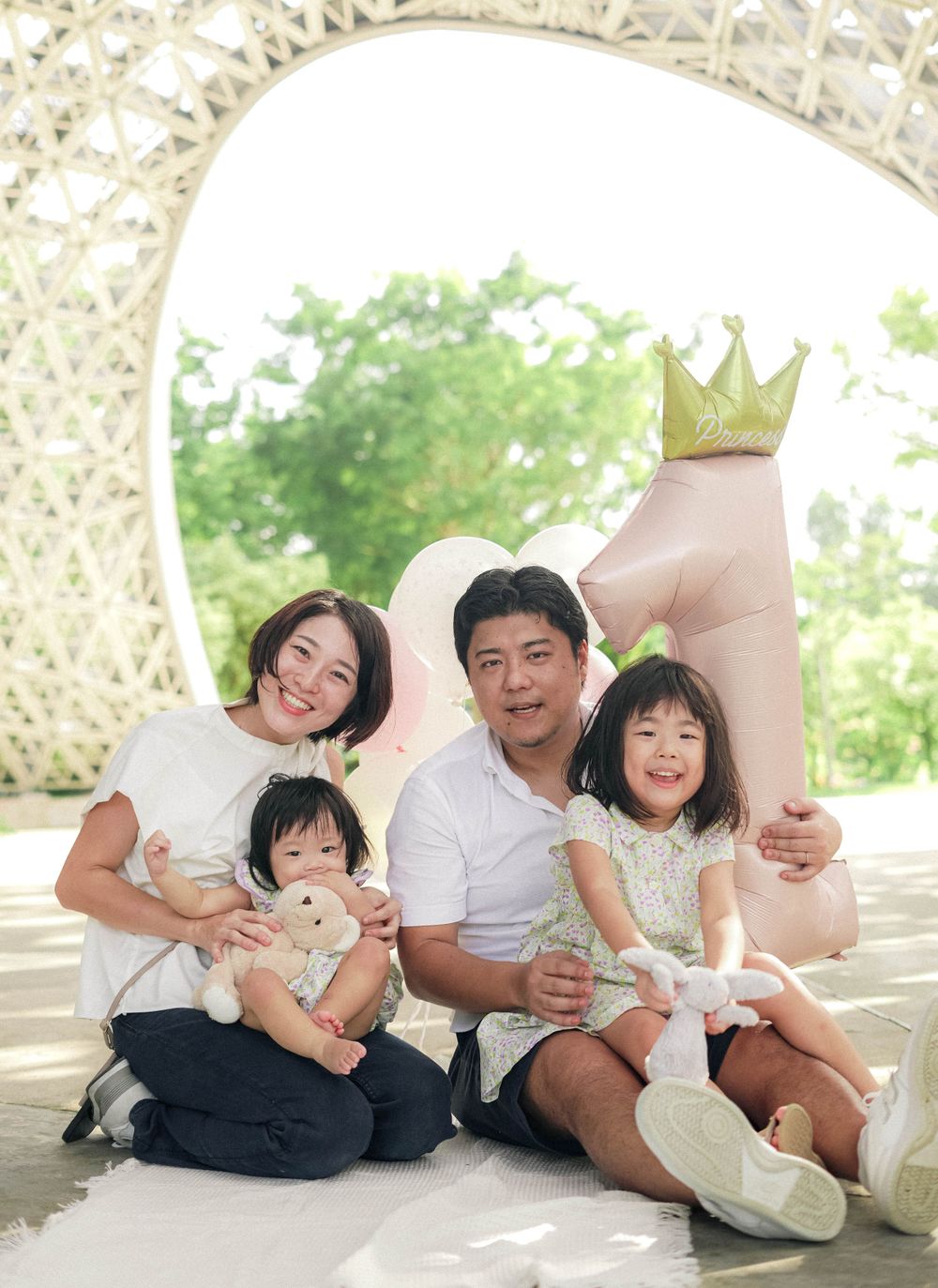 Family portrait under decorative arch with crown prop and stuffed animals.